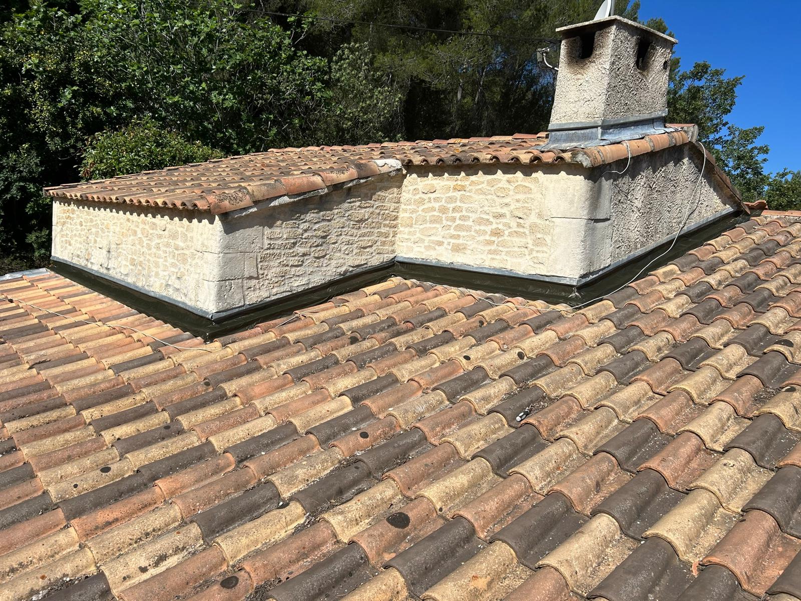 Toit en tuiles canal anciennes au pied d’un mur en pierre, avec des solins neufs posés le long du mur et autour de la cheminée